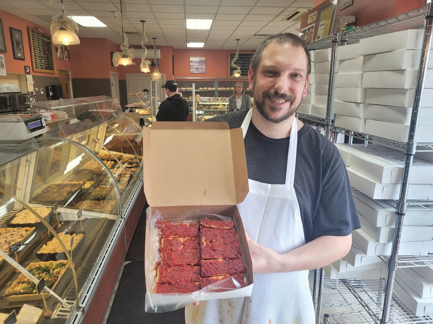 ACQUIRED TASTE: Eric Palmieri, of D. Palmieri’s Bakery in Johnston, holds a box of the shop’s famous pizza strips. Although one famous pizza reviewer said they’re not “his thing,” if you grew up in the Ocean State, chances are  you’ve got strong opinions regarding which bakery serves the best little rectangles. (Beacon Communications photo by Rory Schuler)
